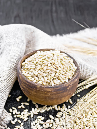 Spelled in a bowl and on the table, stalks with ears of wheat, burlap on the background of wooden boardの写真素材
