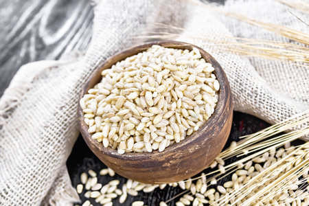 Spelled in a bowl and on the table, stalks with ears of wheat, a burlap napkin on dark wooden board backgroundの写真素材