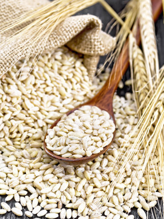 Spelled in a spoon, in a burlap bag and on the table, stalks with ears of wheat on the background of dark wooden boardの写真素材