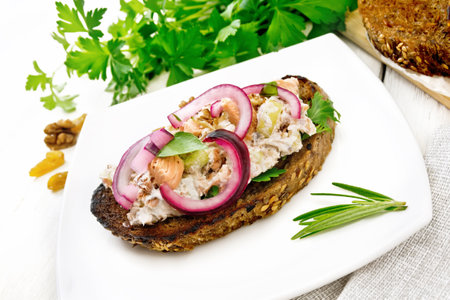 Salad of salmon, petiole celery, raisins, walnuts, red onions and cottage cheese on toasted bread with green lettuce on a plate against light wooden boardの写真素材