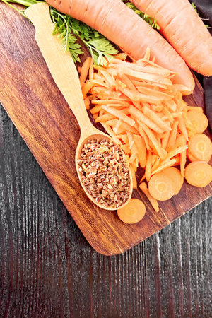 Dried carrots in a spoon, whole with haulm and gratified, napkin on the background of wooden board from aboveの写真素材