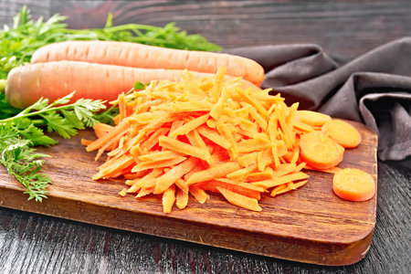 Grated carrots, whole with haulm, sliced, brown napkin on the background of dark wooden boardの写真素材