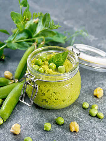 Hummus from green peas and chickpeas in a glass jar, pea pods on granite countertop backgroundの写真素材
