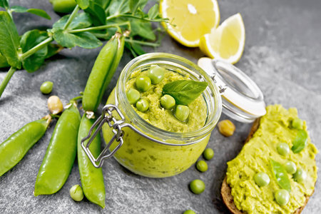 Hummus from green peas and chickpeas in a jar, pea pods, lemon and sandwich on granite countertop backgroundの写真素材