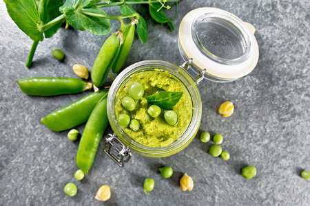 Hummus from green peas and chickpeas in a glass jar, pea pods on top of granite countertop backgroundの写真素材