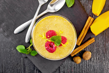 Yogurt, pumpkin and raspberry dessert with nutmeg, cinnamon, orange zest in a glass, vegetable, spoons and spices on a napkin on wooden board background from aboveの写真素材