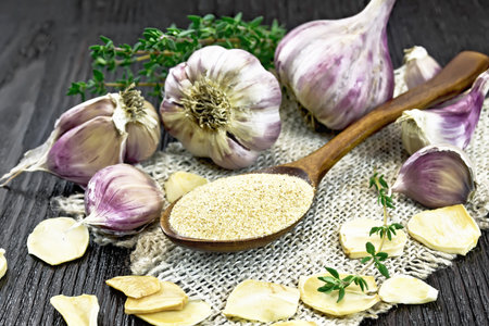 Ground garlic in a spoon on burlap, dried and fresh garlic, bunch of thyme on black wooden board backgroundの写真素材