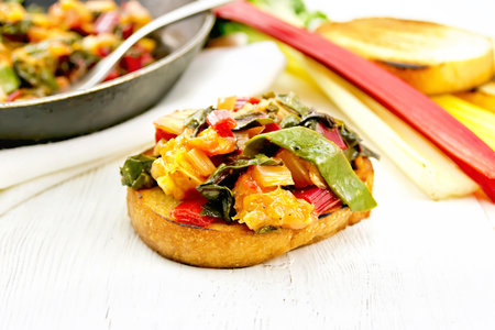 Toasted slice of bread with stewed chard, onion and orange on a wooden table backgroundの写真素材