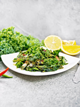 Kale cabbage stewed with orange and hot pepper flakes in a plate on the background of granite countertopの写真素材