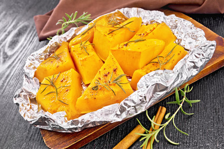 Pumpkin pieces baked in foil with cinnamon and rosemary, brown napkin on dark wooden board backgroundの写真素材