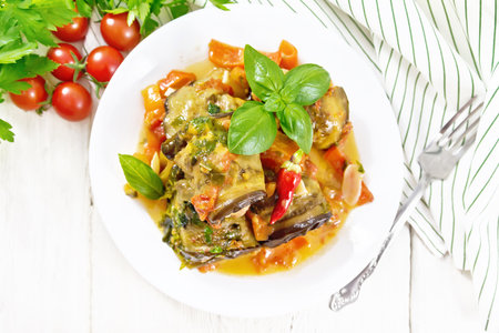 Eggplant rolls with minced meat, tomatoes, garlic, sweet and hot peppers in a plate, napkin, parsley and basil on wooden board background from aboveの写真素材