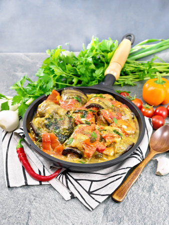 Eggplant rolls with minced meat, tomatoes, garlic, sweet and hot peppers in a frying pan on a towel on the background of stone tableの写真素材
