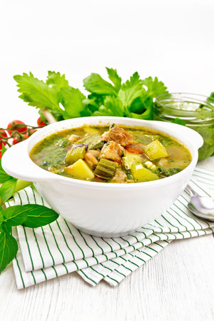Soup with pisto sauce, lard, tomatoes, zucchini, beans, celery and leek in a bowl on a napkin on white wooden board backgroundの写真素材