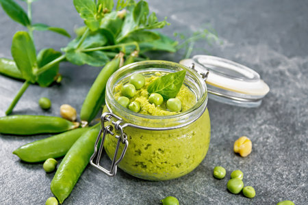 Hummus from green peas and chickpeas in jar, pea pods on background of granite countertopの写真素材