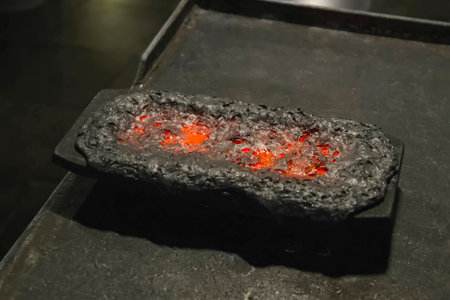 still red with heat, a bar of gold covered with slag in a mold for smelting.