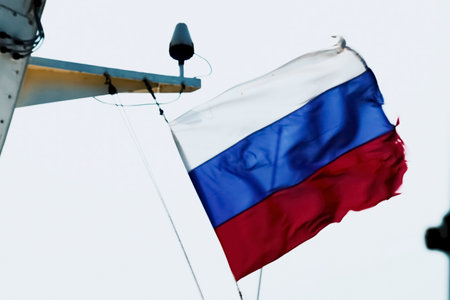 Russian flag with a torn edge against a white sky.の写真素材