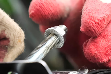 Screwing the nut onto the bolt with a hand in a red glove.の写真素材