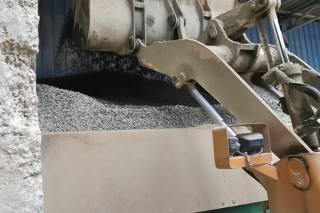 Bulldozer with bucket scooping gravel from a construction base storage for loading