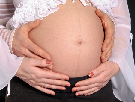The tummy of pregnant woman is embraced by man's armsの写真素材
