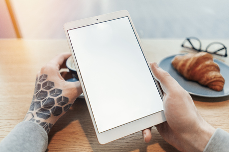 Close up of man tattooed hands holding tablet with blank screen.の写真素材