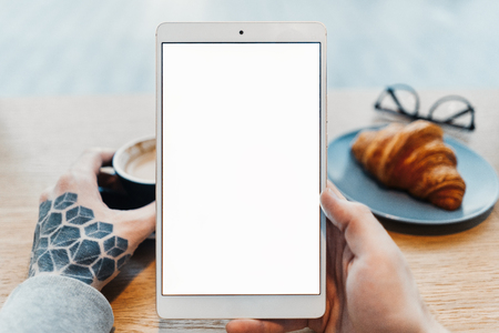 Close up of man tattooed hands holding tablet with blank screen.の写真素材