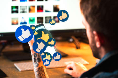 Young Man Holding Modern Mobile Phone With Thumb Up Icons Bursting Out From Screen. Social Media...