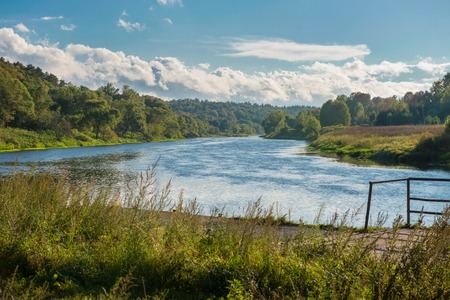 Wide river in green banks overgrown with woodsの写真素材