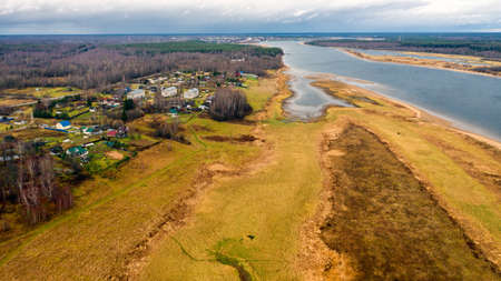 Aerial view of the village on a high hill above the river at sunrise in autumn. aerial view. Residential buildings and a church, river bends, meadows, orange grass, trees at dawn. Colorful aerial landscape of the river coast at sunset in autumn. View from aboveの写真素材