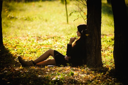 Girl in the hat in autumn park sits under a maple treeの写真素材