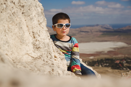 boy sits on the top of rock and look down to Valleyの写真素材