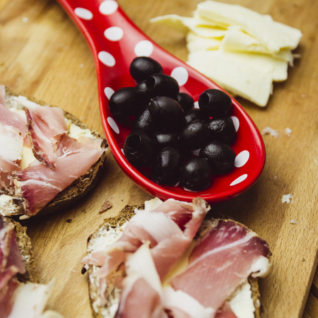 A still-life of olives, goat cheese and homemade smoked meat on a wooden boardの写真素材