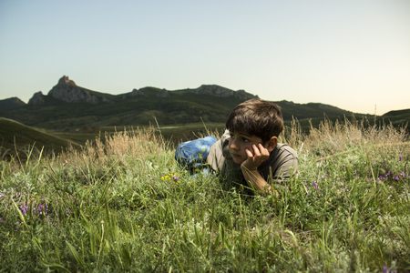 Boy lying in grass at backdrop of the mountainsの写真素材