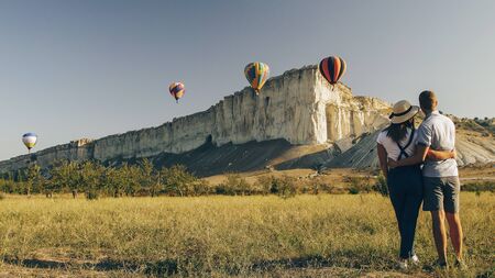 Young couple look at hot air balloons over white rock at dawnの写真素材