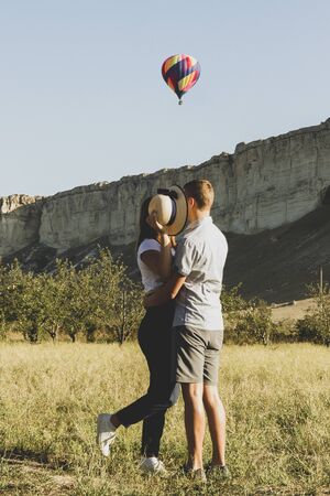 A young couple stands face to face and hides their heads behind a hat. Their dream is balloon soaring above them.の写真素材