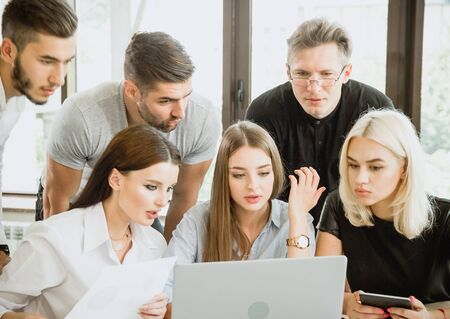 Group of six students with drawings schemes and laptop is working with projectの写真素材