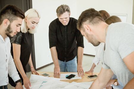 Hard work on the project. All employees and the project manager are standing above the table with documents discussing the project.の写真素材