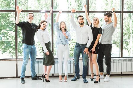 Portrait of six attractive and positive people that is having fun raising hands up bright at vivid trees and office windows backgroundの写真素材