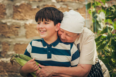 Grandmother hugs her grandson who is holding a corn crop.の写真素材
