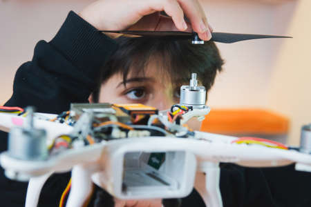 A focused young inventor puts a propeller on a drone. Extracurricular physics work in the home lab.