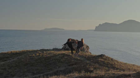 Two women in sportswear and barefoot doing yoga exercises and laughing on the seashore against the...