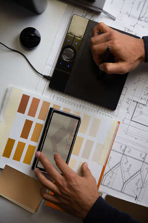 Top view of the interior designers desk. The mans hands work with a graphic tablet and drawings in paper and electronic form.の写真素材