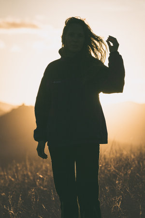 A dark silhouette of a young woman in sportswear with long hair flying in the wind in the rays of the sunset.の写真素材