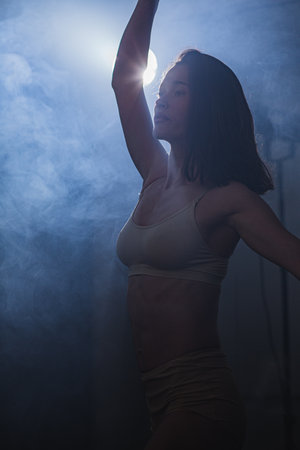 Vertical composition. Ballerina in the studio at rehearsal. Spotlights and fog in blue tones.