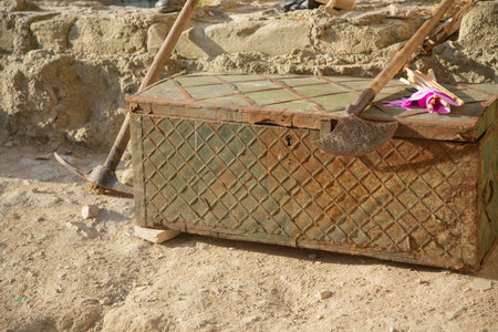 An ancient iron-bound wooden chest with a broken keyhole against a background of stones and excavation tools.の写真素材