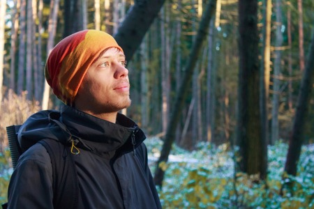 Young man in warm clothing looking up in forestの写真素材