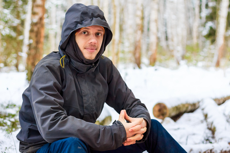 Man traveler sits on a log in winter forest