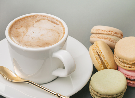 Fresh cappuccino in white cup, spoon on saucer and colorful french macaroons. Copy space.の写真素材