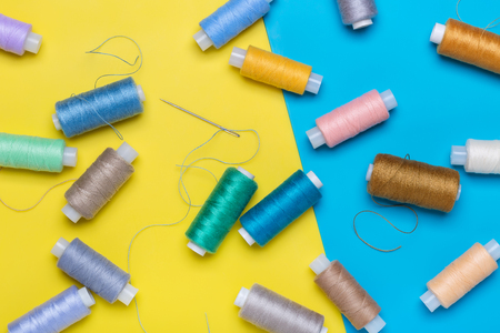 Many coils with multi-colored threads, needle on yellow and blue background.の写真素材