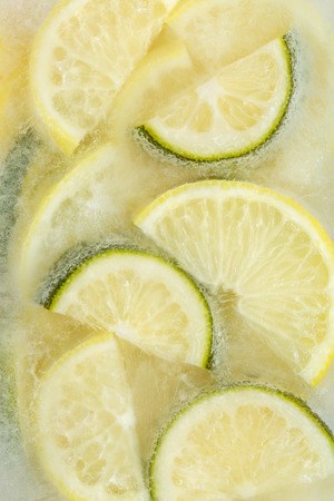 Fresh lemons and lime slices frozen in ice cube on white background. Studio shot.の写真素材