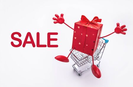 Shopping cart with surprise in red festive box with legs and hands . Discounts, sale. Bright background, copy space.の写真素材
